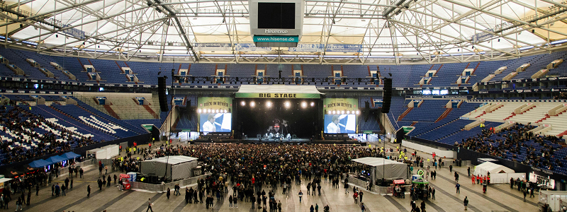 Indoor stadium concert with large stage and audience gathered on the floor