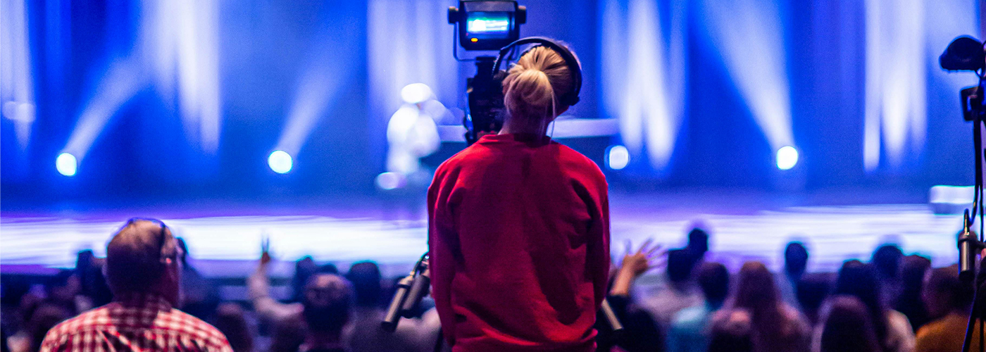 Person on stage presenting to virtual audience with bright lights